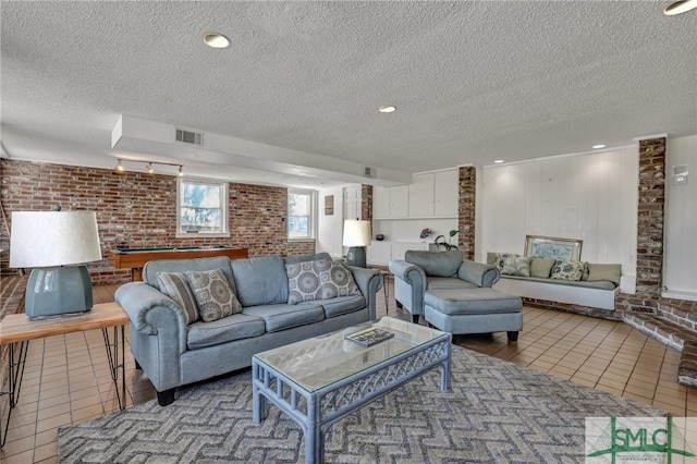 tiled living room with visible vents, billiards, a textured ceiling, and brick wall