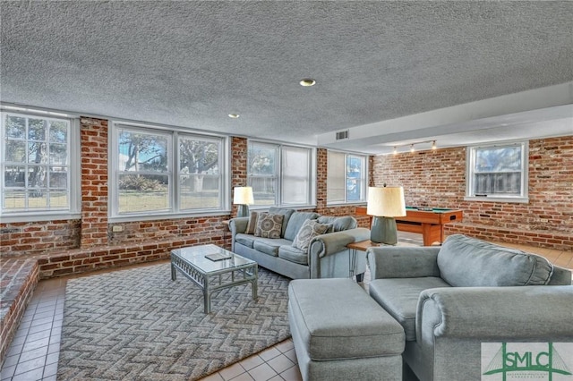 living room featuring a textured ceiling, brick wall, visible vents, and tile patterned floors