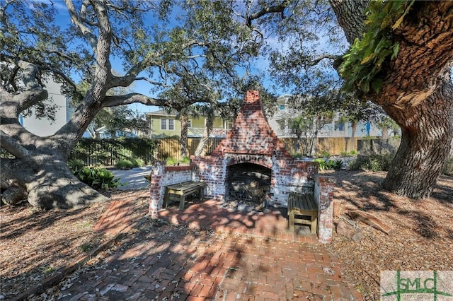 view of yard featuring an outdoor brick fireplace, fence, and a patio