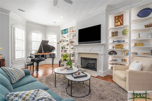 living area featuring visible vents, built in features, wood finished floors, crown molding, and a high end fireplace