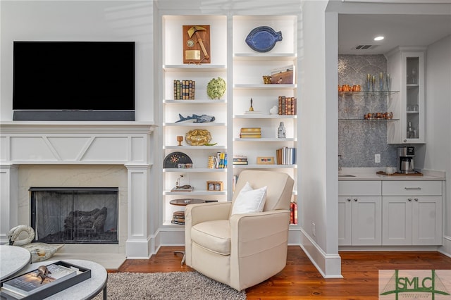 living area featuring visible vents, baseboards, wood finished floors, built in shelves, and a high end fireplace