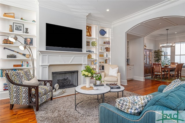 living area featuring built in shelves, arched walkways, crown molding, and wood finished floors