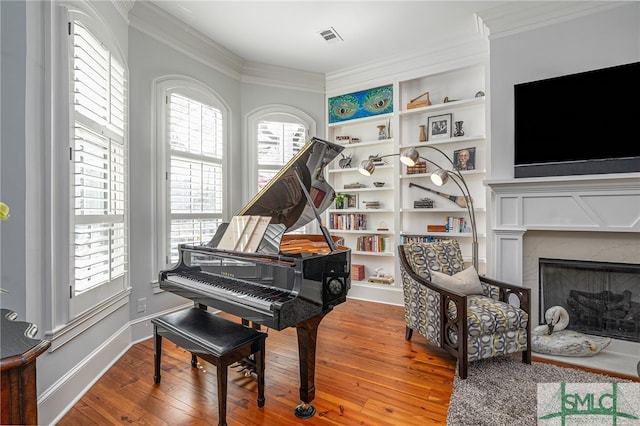 sitting room with visible vents, hardwood / wood-style flooring, built in shelves, ornamental molding, and a fireplace