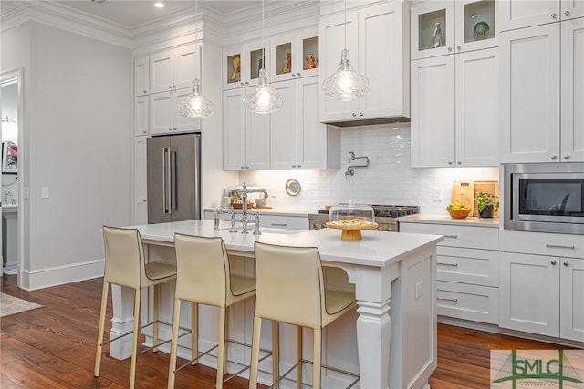 kitchen featuring stainless steel appliances, ornamental molding, tasteful backsplash, dark wood finished floors, and a center island with sink