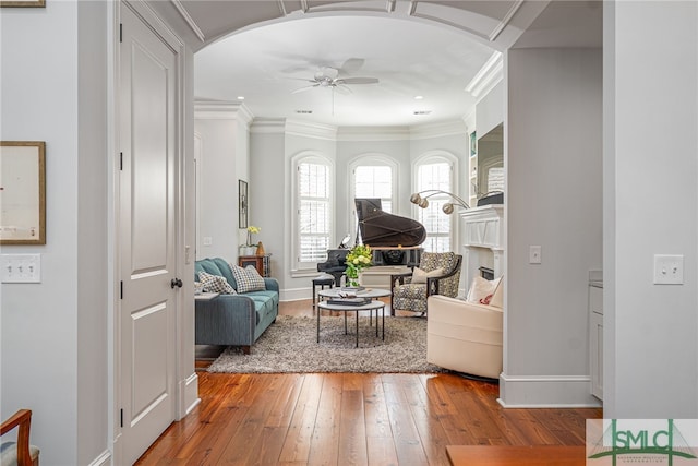 interior space featuring arched walkways, baseboards, hardwood / wood-style flooring, ceiling fan, and ornamental molding