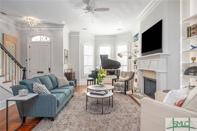 living room with a fireplace, wood finished floors, visible vents, ornamental molding, and stairway