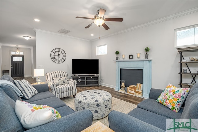 living room featuring a fireplace with flush hearth, wood finished floors, visible vents, ornamental molding, and a wealth of natural light