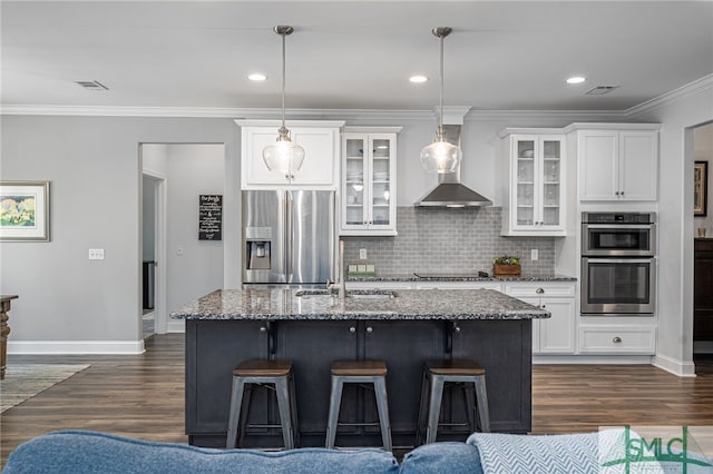 kitchen with dark stone counters, wall chimney exhaust hood, dark wood-type flooring, stainless steel appliances, and backsplash