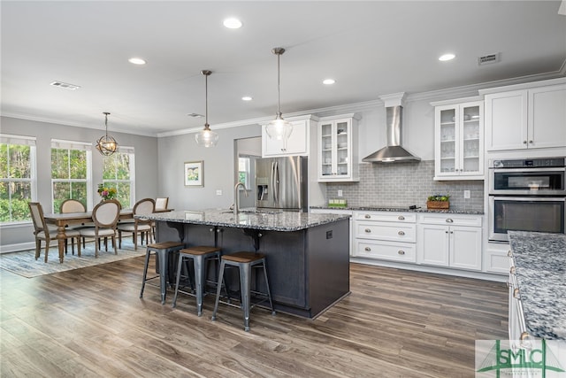 kitchen featuring crown molding, visible vents, appliances with stainless steel finishes, white cabinetry, and wall chimney exhaust hood