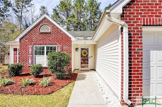 view of exterior entry with a garage and brick siding