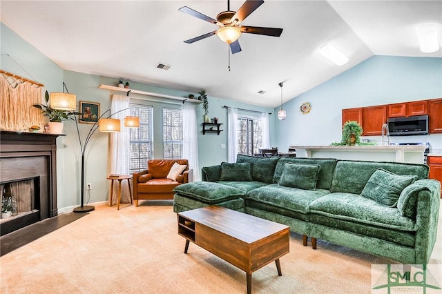 living room with visible vents, light colored carpet, ceiling fan, vaulted ceiling, and a fireplace