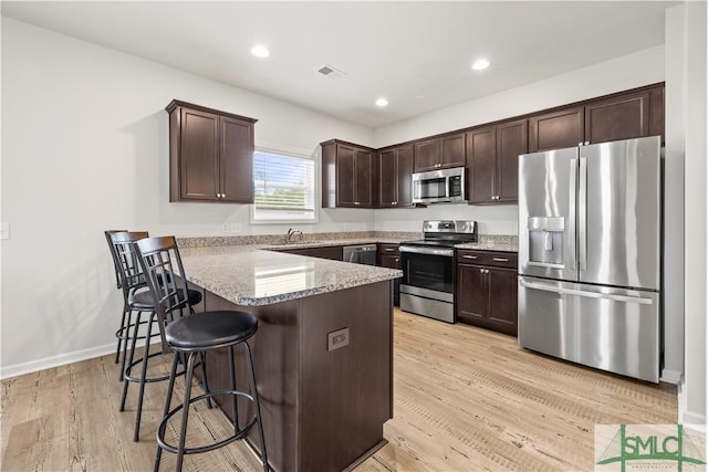 kitchen featuring a peninsula, a breakfast bar, dark brown cabinets, appliances with stainless steel finishes, and light wood finished floors