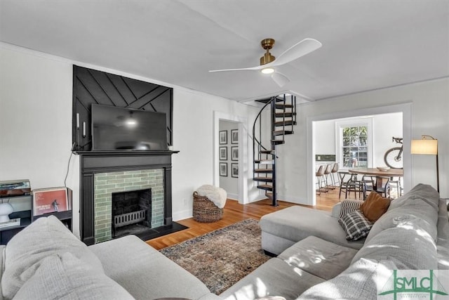 living area featuring a fireplace, stairway, a ceiling fan, wood finished floors, and baseboards