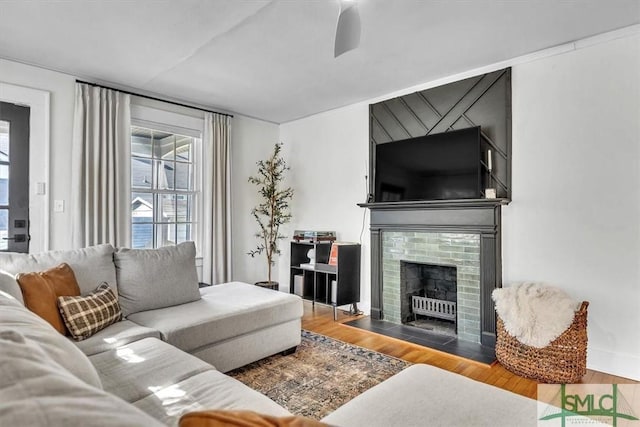 living area with a fireplace with flush hearth, wood finished floors, a ceiling fan, and a healthy amount of sunlight