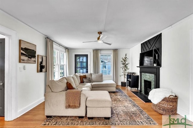 living room featuring a large fireplace, ceiling fan, baseboards, and wood finished floors