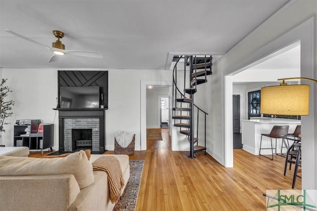 living area with light wood finished floors, stairway, a brick fireplace, ceiling fan, and baseboards