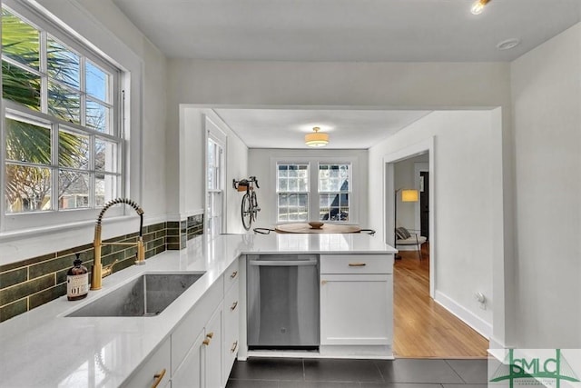 kitchen featuring white cabinets, a peninsula, light countertops, stainless steel dishwasher, and a sink