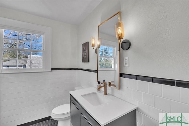 bathroom with toilet, a wainscoted wall, vanity, and tile walls