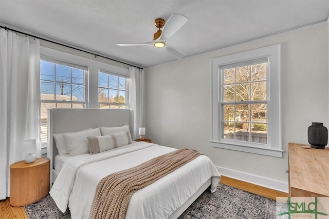 bedroom featuring a ceiling fan, multiple windows, baseboards, and wood finished floors