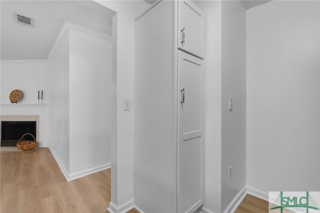 corridor featuring ornamental molding, light wood-type flooring, visible vents, and baseboards