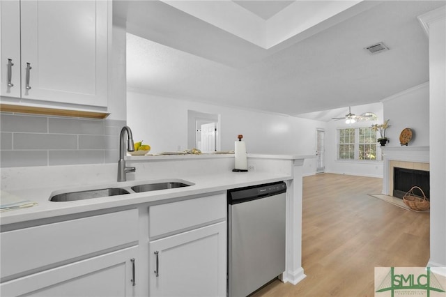 kitchen featuring a fireplace with raised hearth, a peninsula, a sink, stainless steel dishwasher, and tasteful backsplash