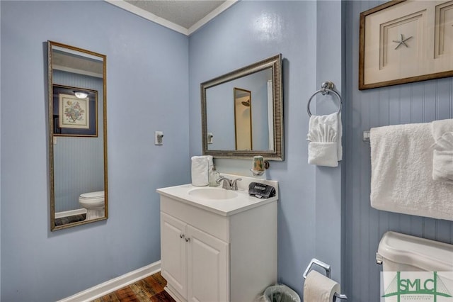 bathroom featuring crown molding, toilet, vanity, wood finished floors, and baseboards