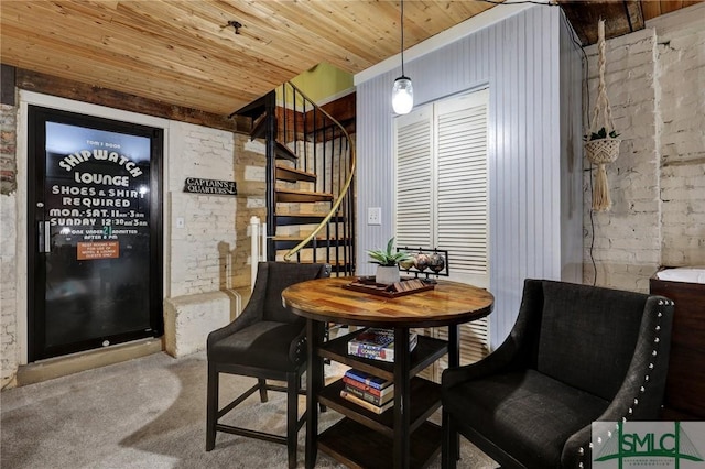 dining room featuring carpet floors, wooden ceiling, brick wall, and stairs