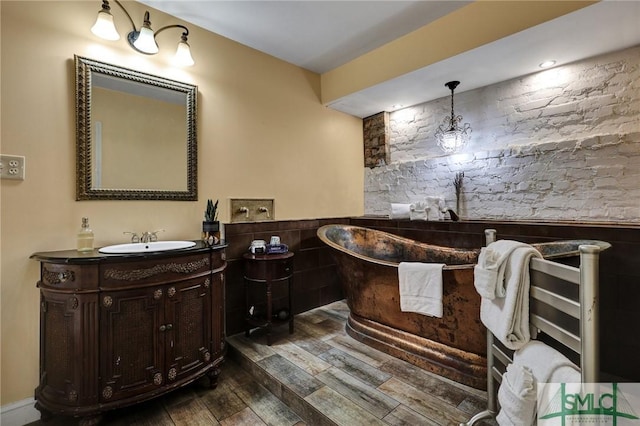 bathroom featuring a wainscoted wall, a soaking tub, wood finished floors, and vanity