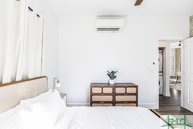 bedroom featuring stacked washer and dryer, baseboards, a wall unit AC, ceiling fan, and wood finished floors