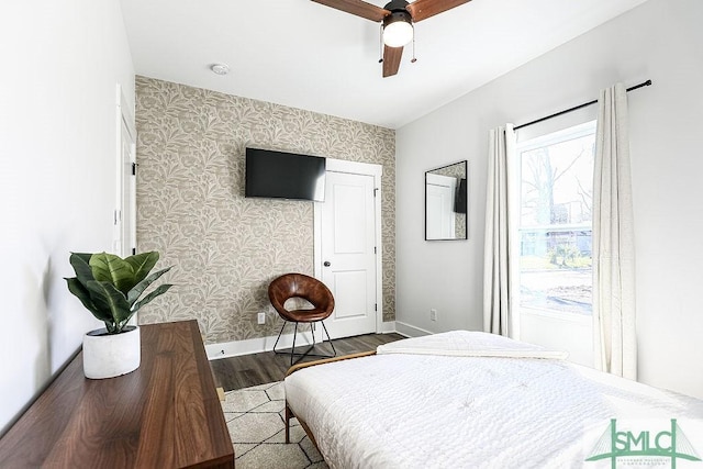 bedroom with wood finished floors, ceiling fan, baseboards, and wallpapered walls