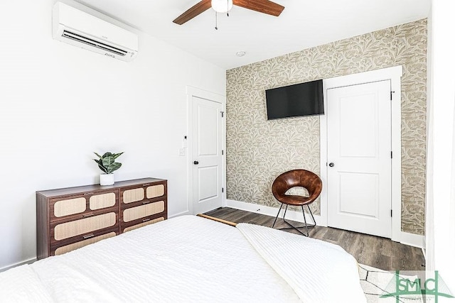 bedroom with a wall unit AC, wallpapered walls, baseboards, and wood finished floors