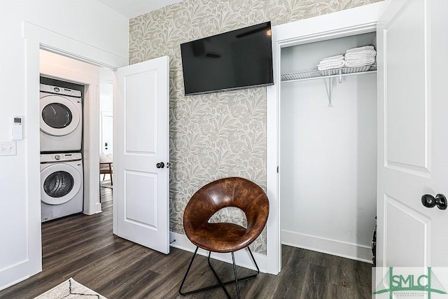 clothes washing area featuring laundry area, dark wood-type flooring, baseboards, stacked washer / drying machine, and wallpapered walls