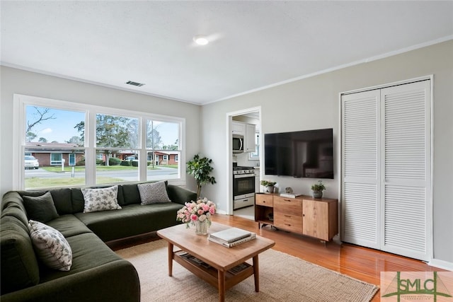 living room featuring light wood-style floors, baseboards, visible vents, and ornamental molding