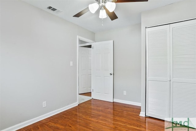 unfurnished bedroom with a closet, visible vents, a ceiling fan, wood finished floors, and baseboards