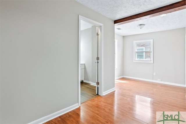 spare room with visible vents, baseboards, a textured ceiling, light wood-style floors, and beam ceiling