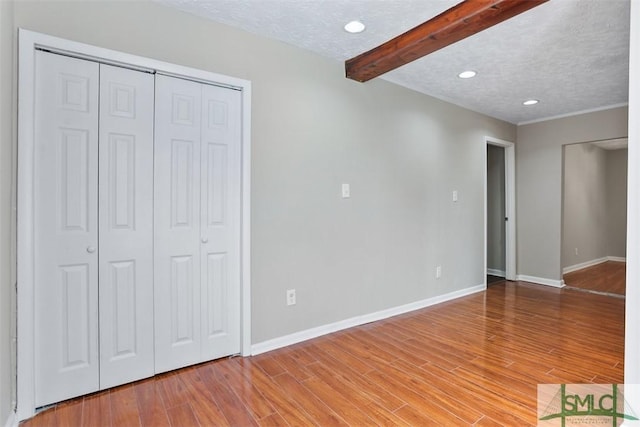 unfurnished bedroom featuring a textured ceiling, light wood finished floors, beam ceiling, and baseboards