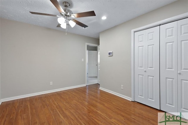 unfurnished bedroom with a closet, a ceiling fan, a textured ceiling, wood finished floors, and baseboards