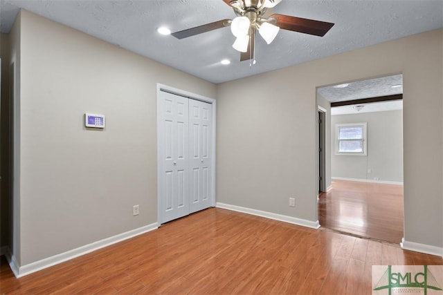 unfurnished room with light wood-type flooring, a ceiling fan, baseboards, and a textured ceiling