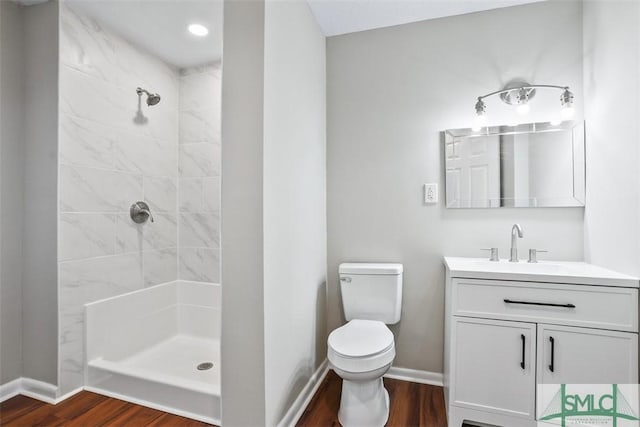 bathroom with toilet, wood finished floors, tiled shower, and vanity