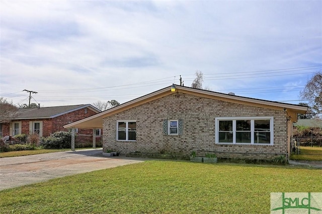 view of side of property featuring a yard, concrete driveway, brick siding, and a carport