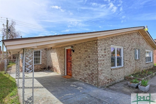 exterior space featuring a carport, concrete driveway, brick siding, and fence