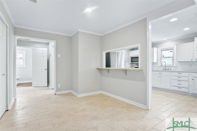 kitchen with stainless steel appliances, white cabinetry, light countertops, light wood finished floors, and crown molding