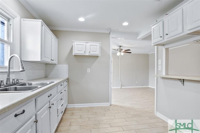 kitchen featuring a sink, a ceiling fan, white cabinets, light countertops, and backsplash