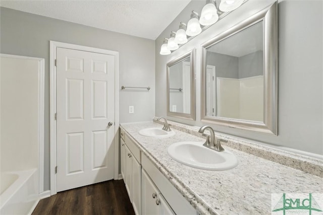 full bath with double vanity, a tub, a sink, and wood finished floors