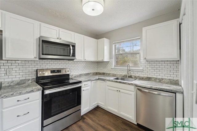 kitchen with stainless steel appliances, dark wood-style flooring, a sink, white cabinets, and tasteful backsplash