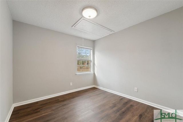 empty room featuring a textured ceiling, dark wood-style flooring, attic access, and baseboards