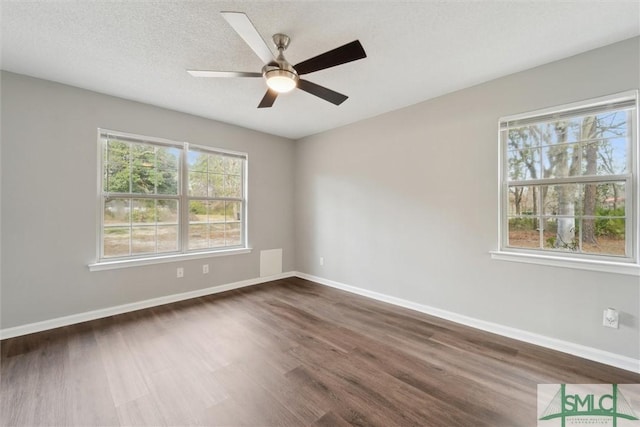 spare room with a textured ceiling, dark wood-type flooring, visible vents, a ceiling fan, and baseboards