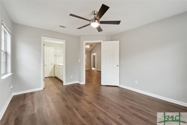 unfurnished bedroom featuring connected bathroom, dark wood-style flooring, a ceiling fan, visible vents, and baseboards