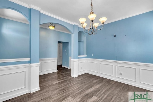 unfurnished room featuring an inviting chandelier, arched walkways, wainscoting, and wood finished floors