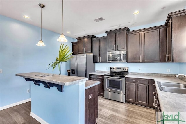 kitchen with dark brown cabinetry, a kitchen island, a sink, light wood finished floors, and appliances with stainless steel finishes